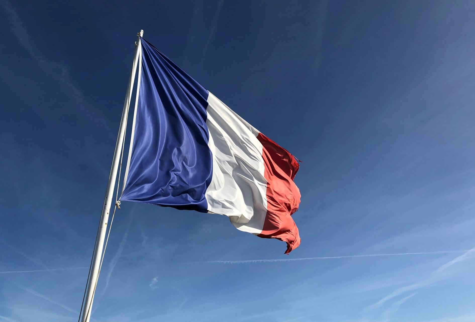 Couleur du drapeau français flottant au vent au sommet d'un mât, au fond le ciel en camaïeu de bleu.